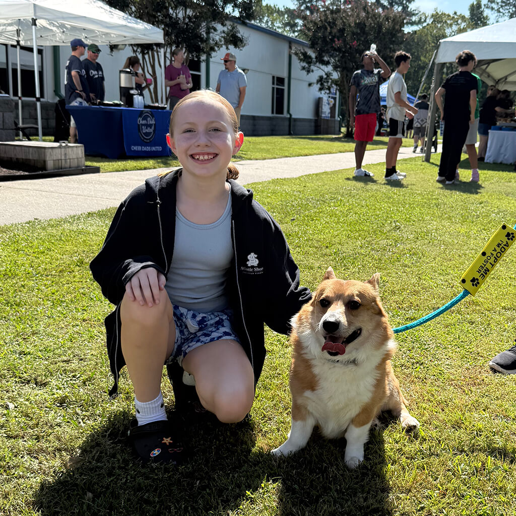 Girl kneels next to a Corgi mix in the grass